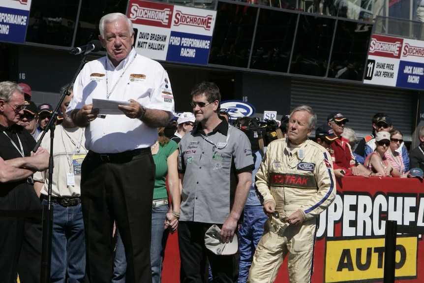 Reverend Coleman wearing a white shirt while addressing Bathurst 1000, with crowd and drivers in background