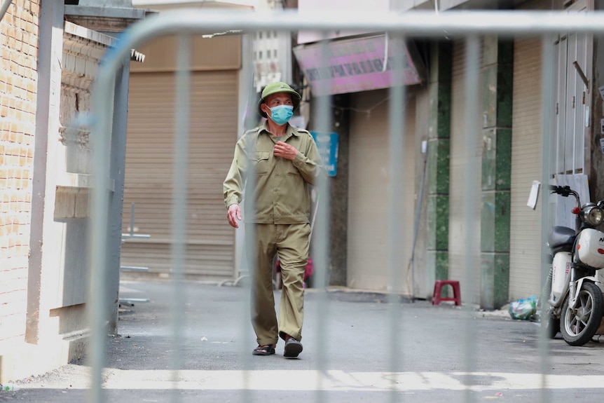 A militia officer patrols a barricaded alley after one of its residents is suspected to have COVID-19 in Hanoi.