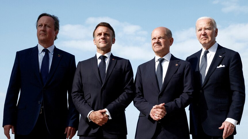 Four white men in navy blue suits all stand beside each other.