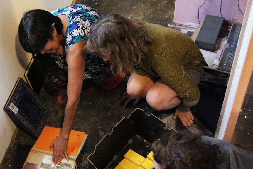 Image of three women looking at a photo album on the ground.