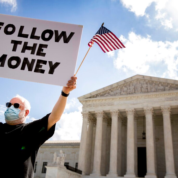 A protester holds up a "Follow the Money" sign with an American flag outside the Supreme Court in Washington DC