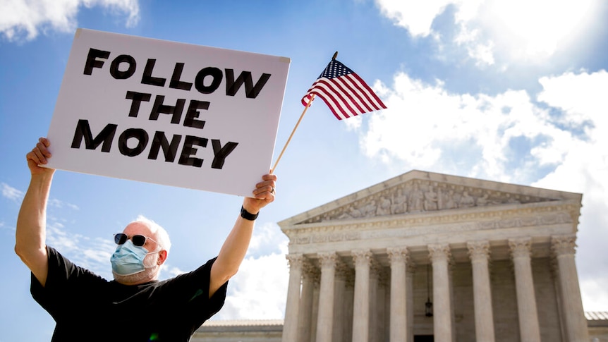 A protester holds up a "Follow the Money" sign with an American flag outside the Supreme Court in Washington DC
