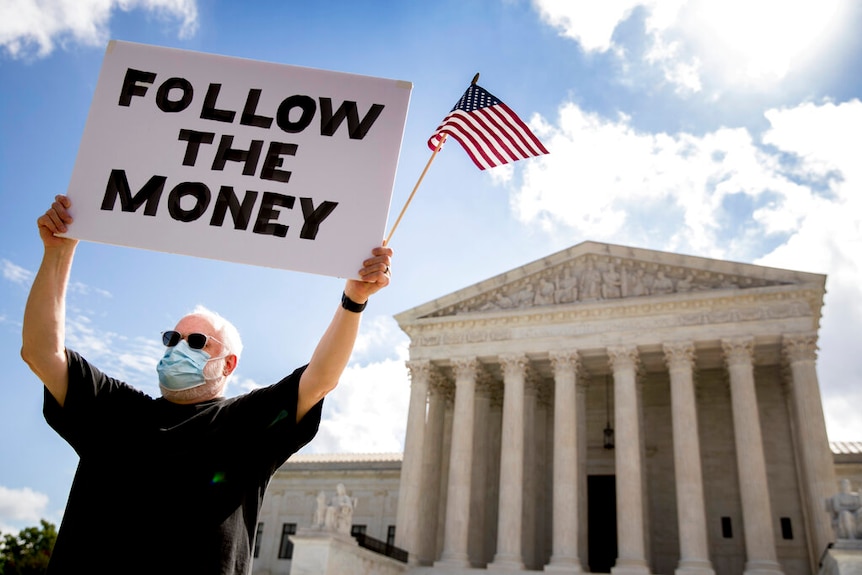 A protester holds up a "Follow the Money" sign with an American flag outside the Supreme Court in Washington DC