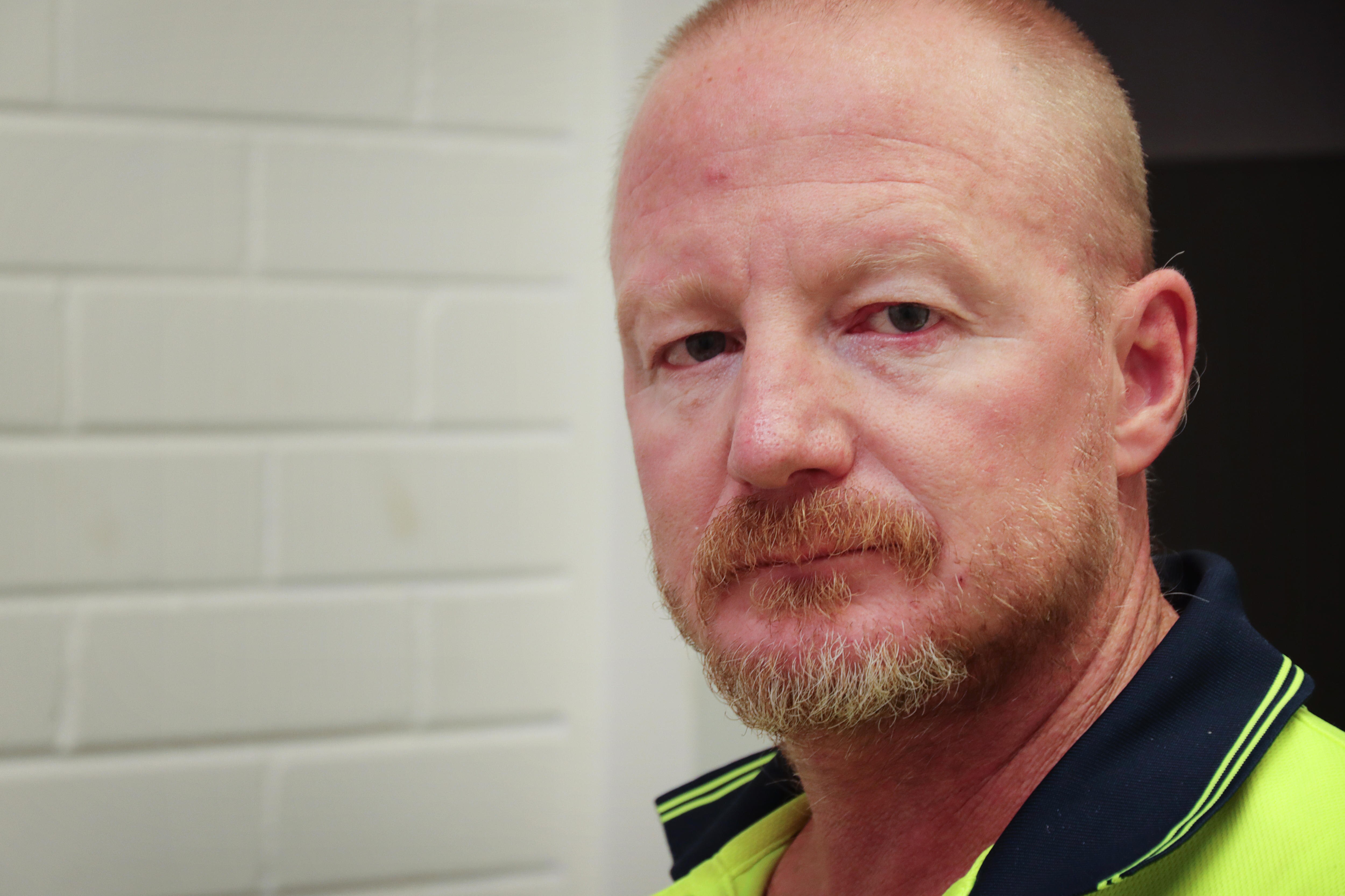 Corey Reichstein looks at the camera from close range with a white wall behind him.