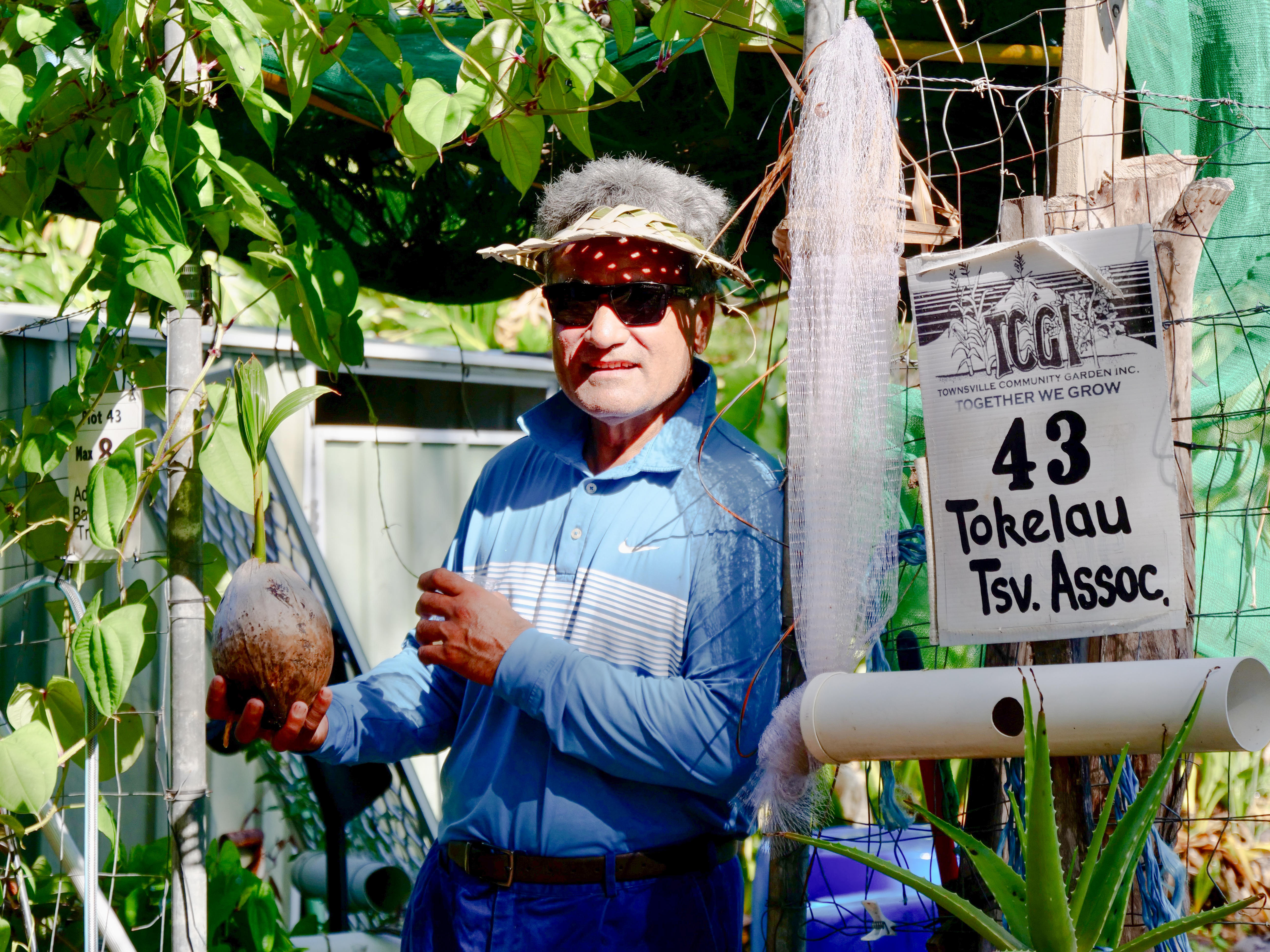 Hombre de la isla del Pacífico sosteniendo coco fresco con brotes mientras se apoya en la valla del jardín.