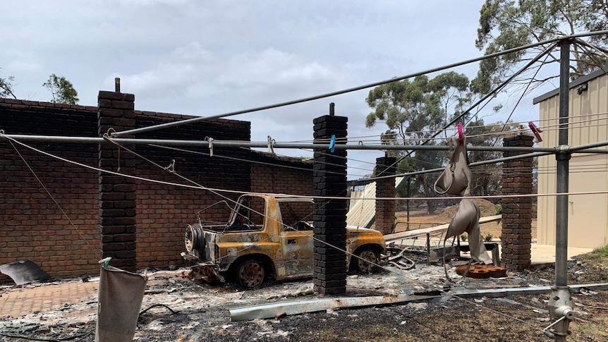 A burnt car and house with a clothes line in the foreground