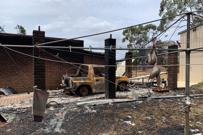 A burnt car and house with a clothes line in the foreground