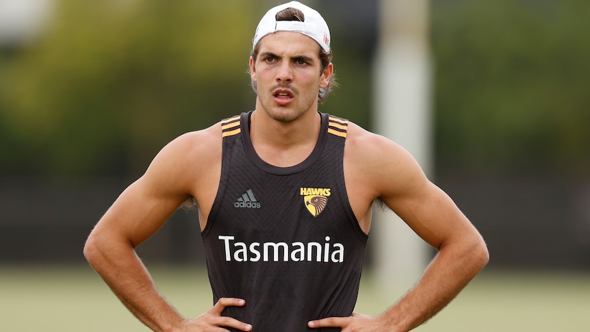 A Hawthorn AFL player stands with his hands on his hips during a training session.