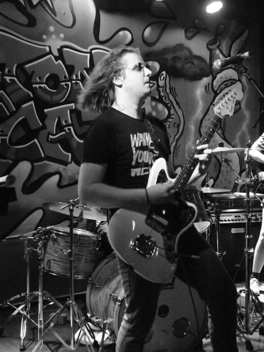 A black and white photo of Alex Carrette performing on stage with his guitar