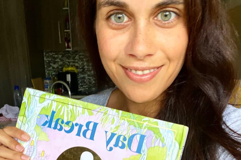 Amy McQuire, light green eyes, brown hair, holds her colourful children's book called Day Break.
