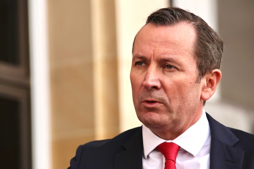WA Premier Mark McGowan wearing a dark suit, white shirt, and red tie, outside parliament in Perth.