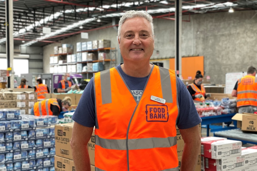 A man standing in a busy warehouse, wearing a Food Bank high-vis vest.