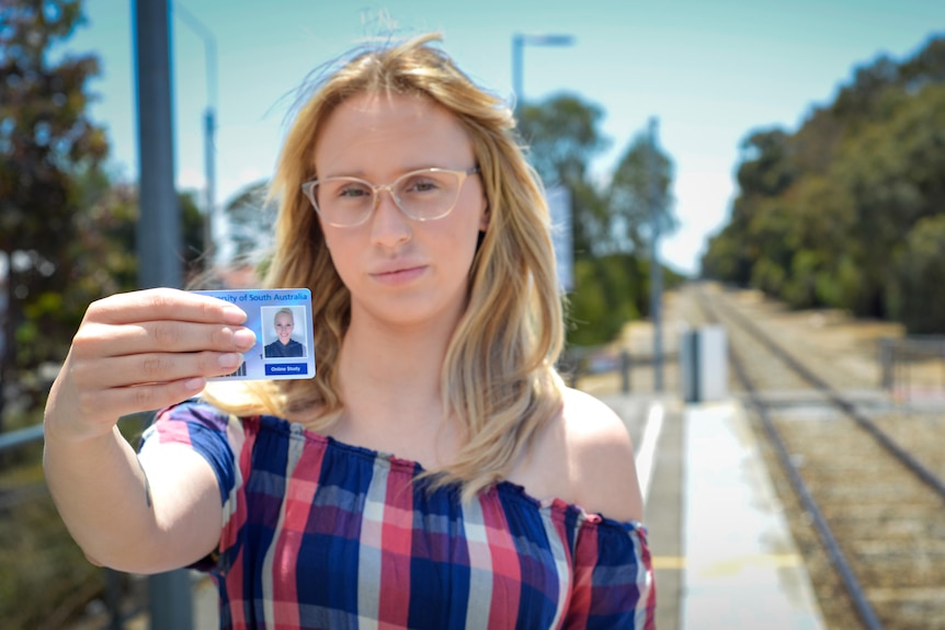 A young woman holds up her student card.
