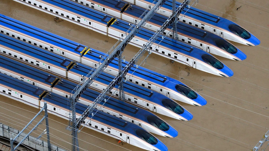 A group of trains are surrounded by muddy floodwaters, as seen from above in a helicopter.