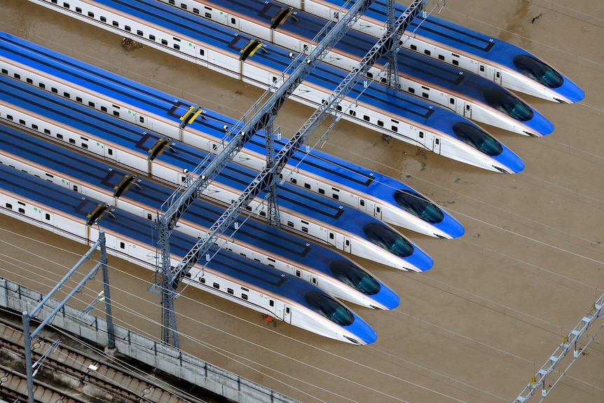 A group of trains are surrounded by muddy floodwaters, as seen from above in a helicopter.