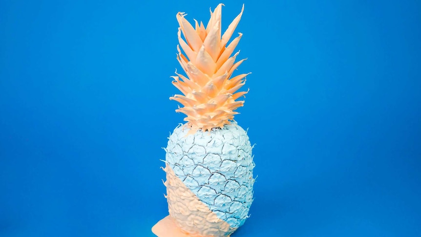 A pineapple painted in apricot and pale blue colours for a dramatic contrast against a vivid blue background.