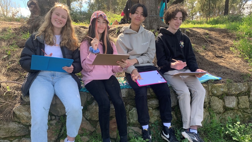 Four high school students sit outdoors with pen and paper