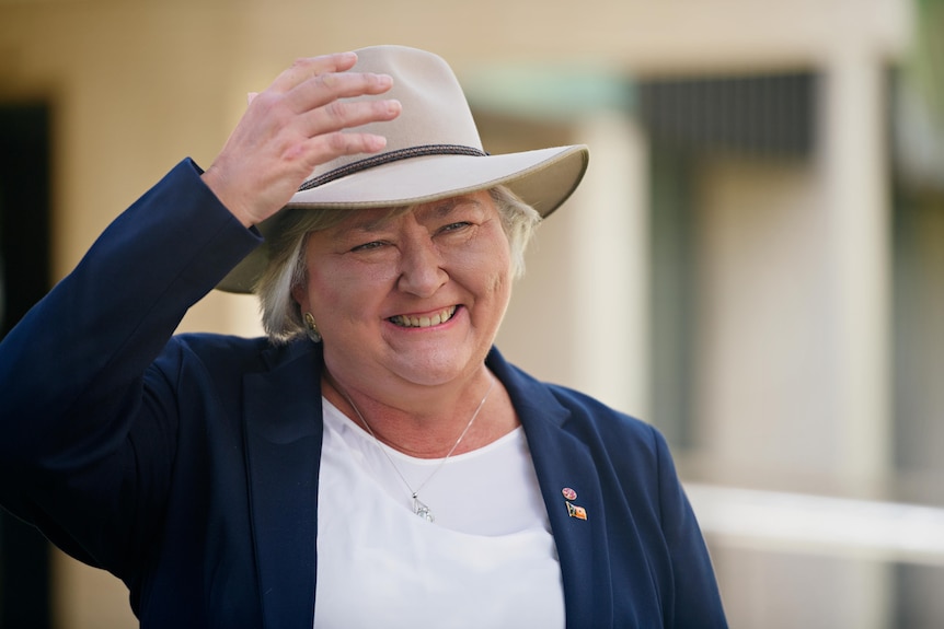 Sam McMahon smiles while holding her hat on her head at a press conference.