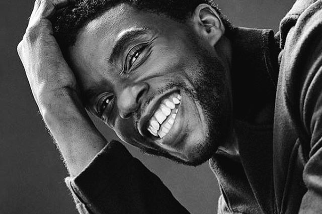 A black and white photograph of Chadwick Boseman smiling.