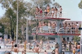 A 1979 photo of a two-tier diving platform packed with people in board shorts and bikinis. 