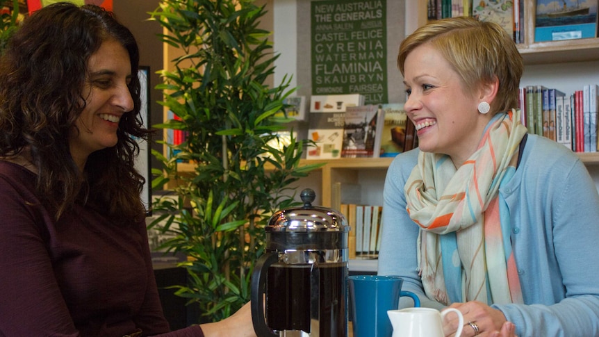 Two women smile at each other while drinking coffee