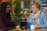 Two women smile at each other while drinking coffee
