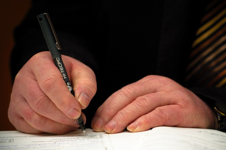 A man's hand holding a pen, signing paperwork.