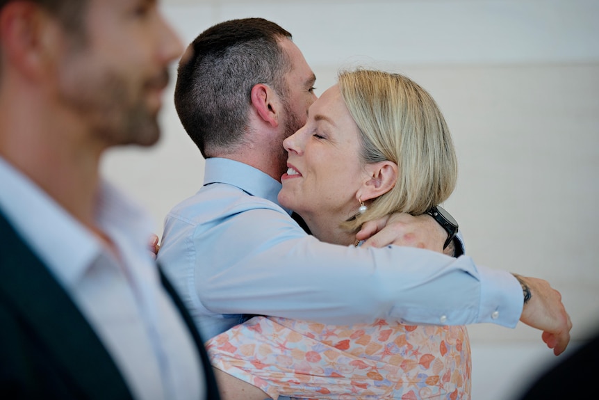 a man with close cropped hair hugs a blonde woman