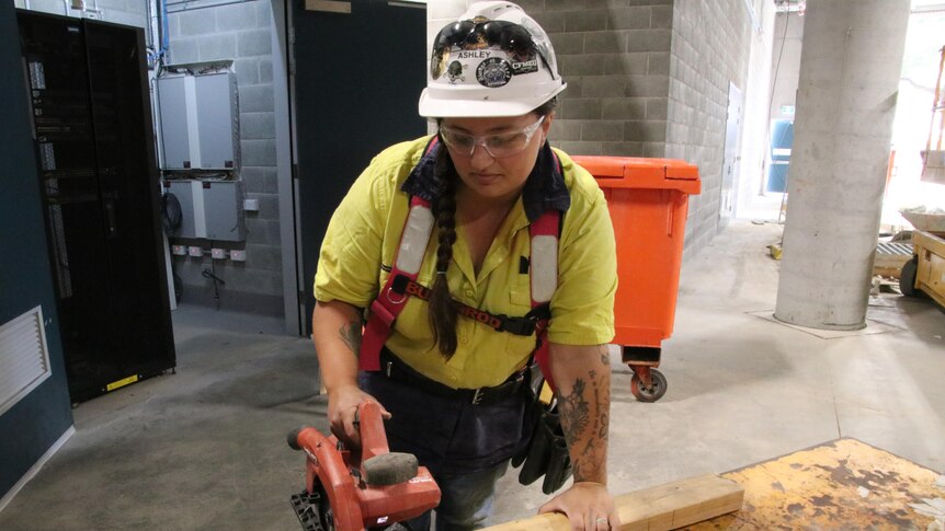 a woman holding a saw and wearing a hard hat