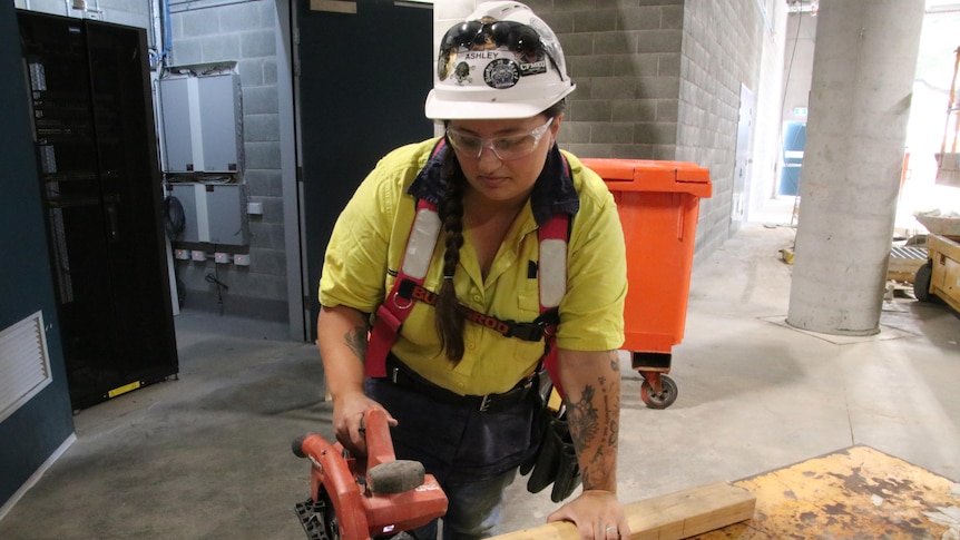 a woman holding a saw and wearing a hard hat