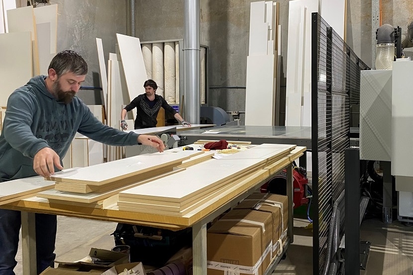 Two men in a workshop shifting pieces of kitchen cabinetry.