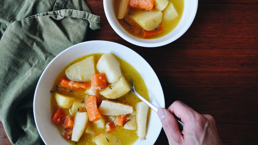 Two bowls of carrot, potato and parsnip stew, on a dining table, alongside a green linen napkin, a winter family dinner recipe.