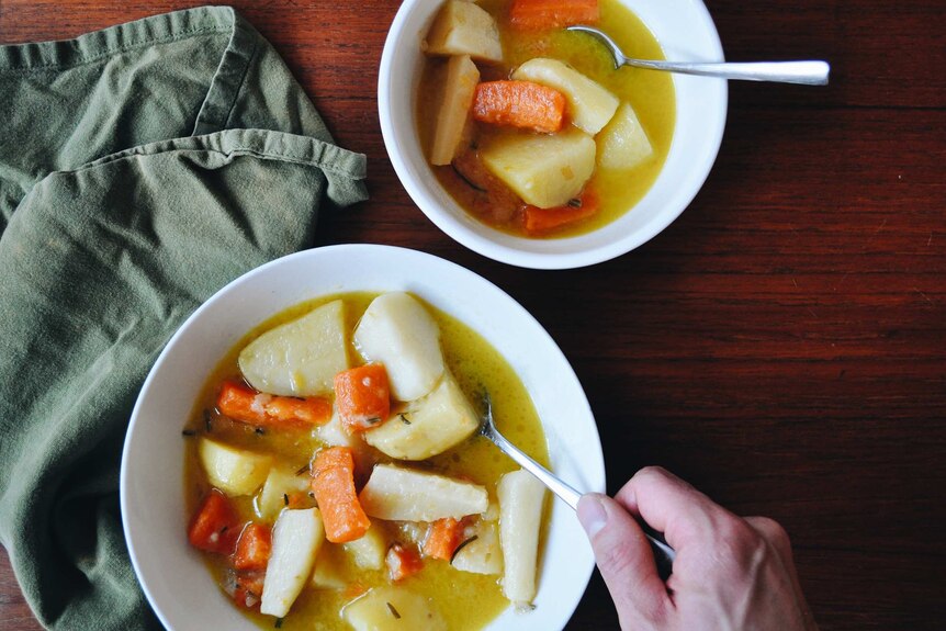 Two bowls of carrot, potato and parsnip stew, on a dining table, alongside a green linen napkin, a winter family dinner recipe.