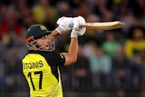 A man in a green and yellow Australian T20 cricket uniform lifts his bat high over his shoulder during a shot.