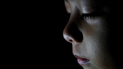 A close-up portrait of a boy with his eyes closed, in front of darkness.