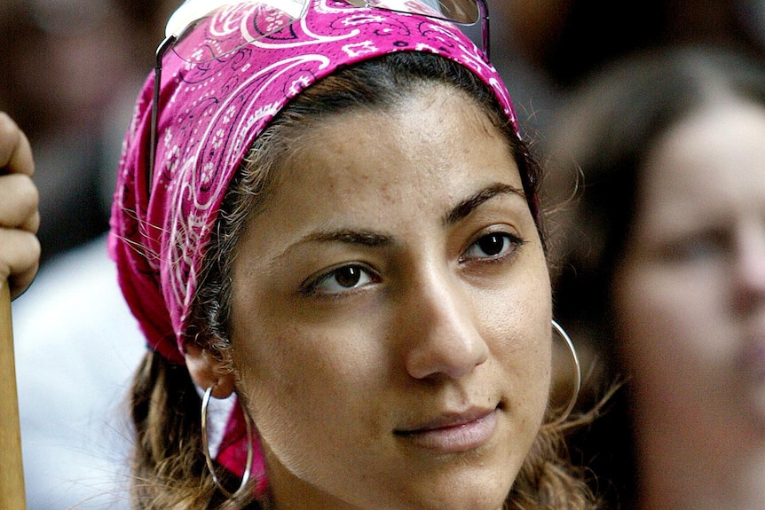 Girl listening during protests wearing hand-made anti-war singlet, hoop earrings and pink bandana 
