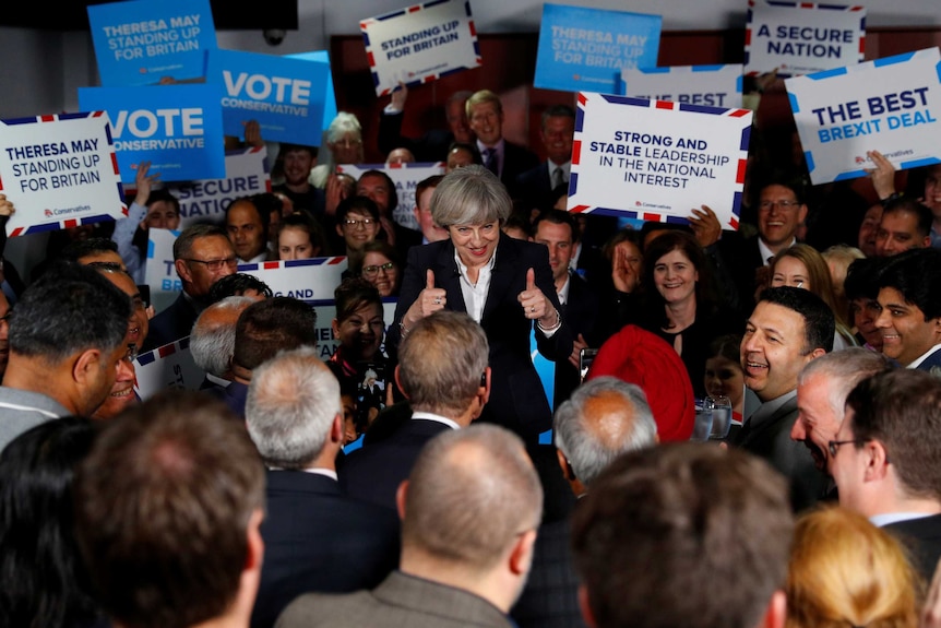 Theresa May gives the thumbs up surrounded by supporters holding up posters.