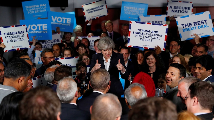 Theresa May gives the thumbs up surrounded by supporters holding up posters.