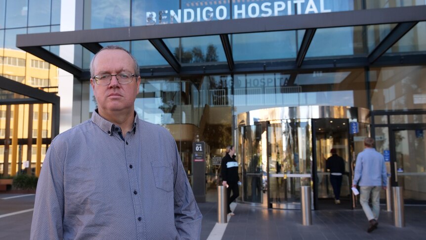 A man standing outside revolving doors.