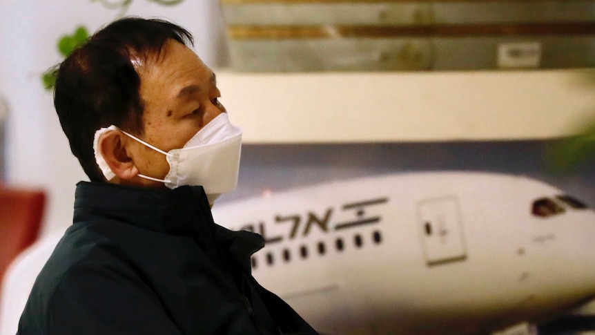 An Asian man is seated in an airport wearing a face mask