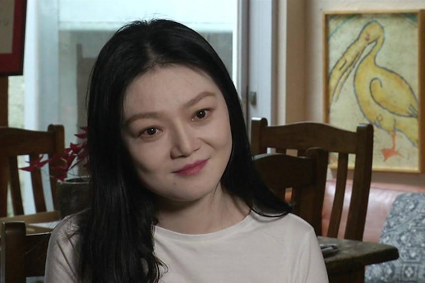 A woman with long dark hair is calmly looking at the camera.