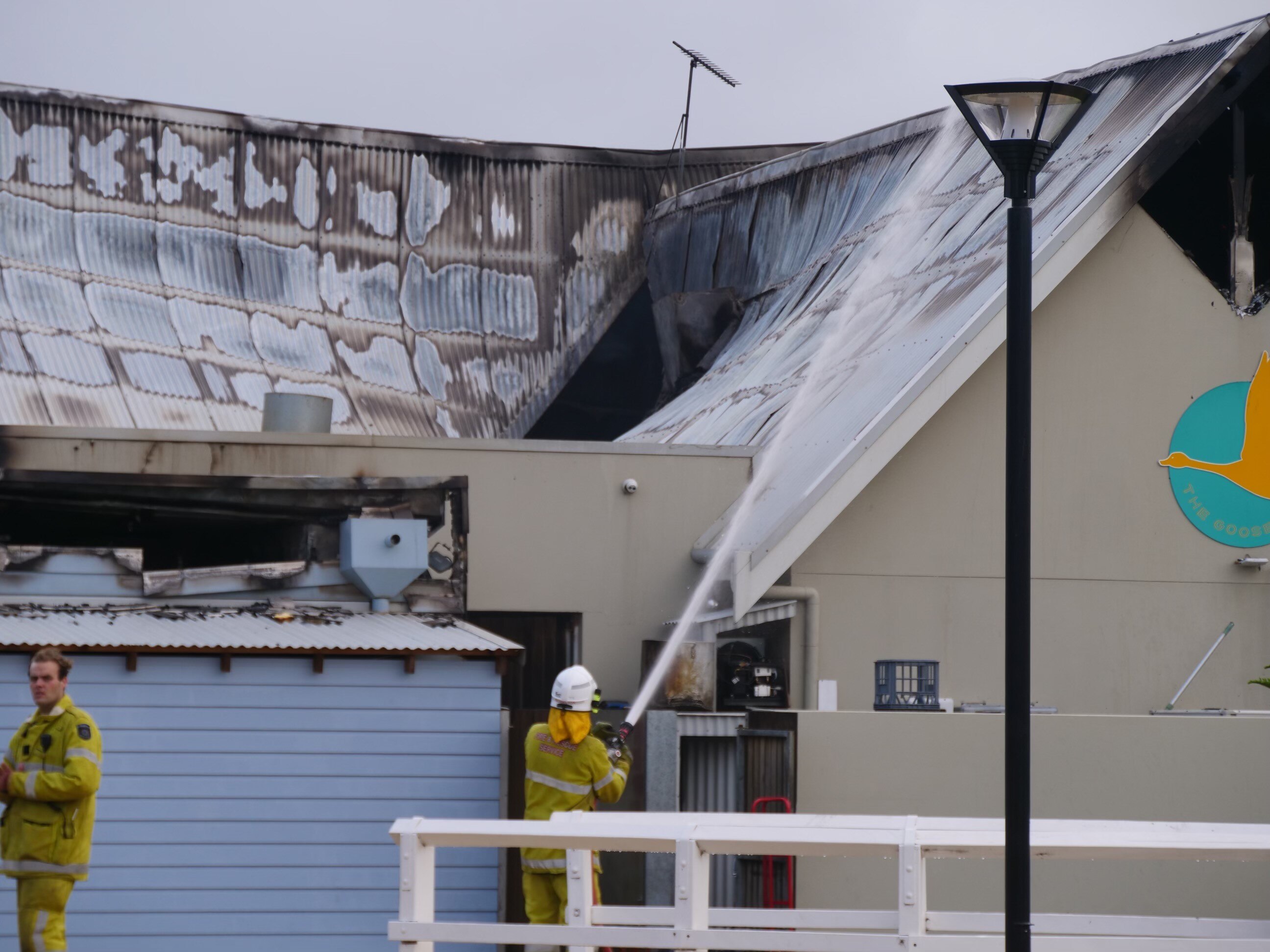 A firefighter squirting the roof of a restaurant with a visible hole in the top after a fire burnt through.