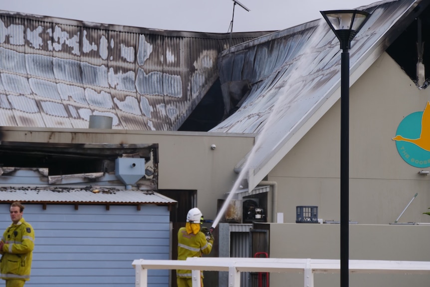 A firefighter squirting the roof of a restaurant with a visible hole in the top after a fire burnt through.