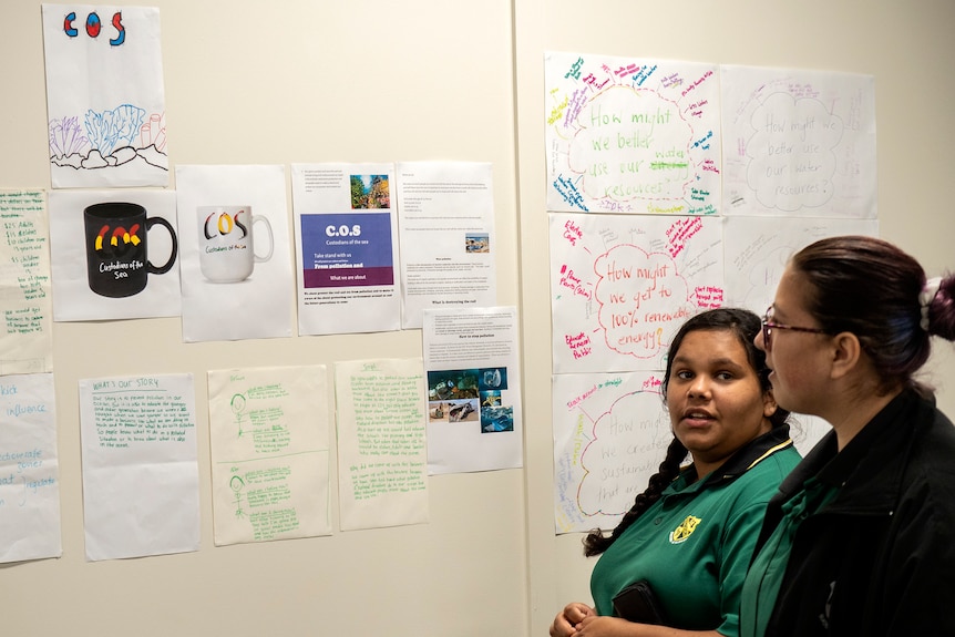 Two students look at a board filled with random text.