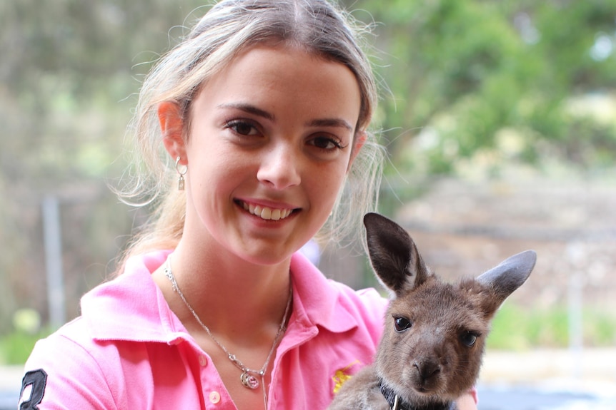 A young woman has a small kangaroo in her arms