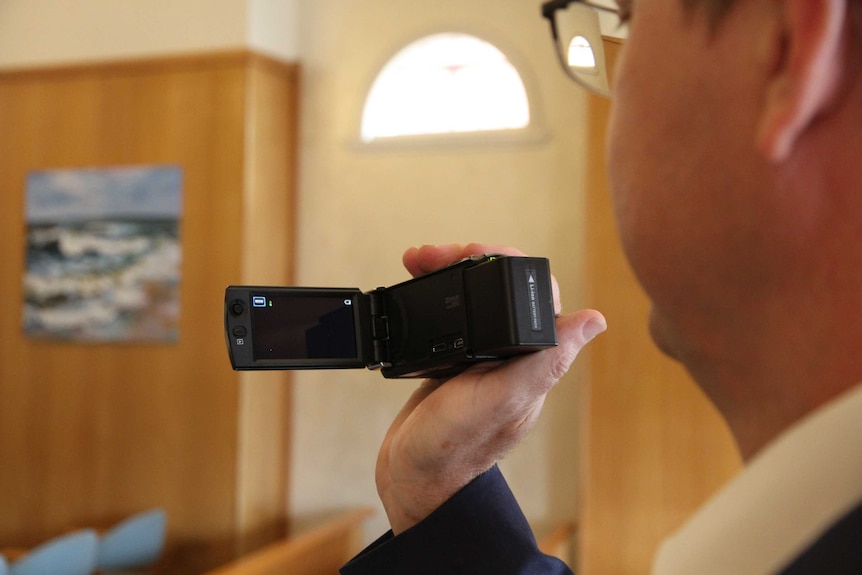 A man looks at the viewfinder of a small handheld video camera.