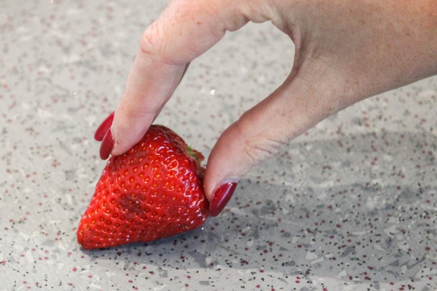 A woman picks up a strawberry from the floor.