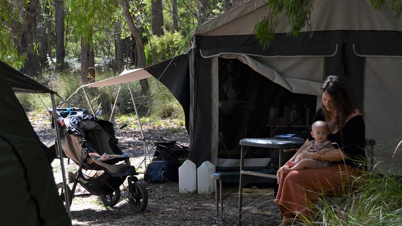 Woman holding her baby by the tent in the bush