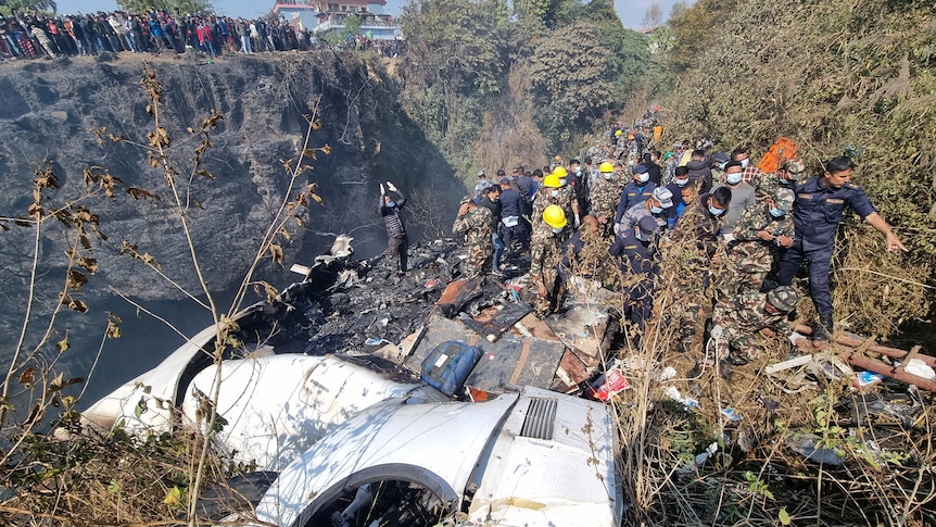 Plane crash in Nepal with 72 onboard. Workers inspect the crash site and debris