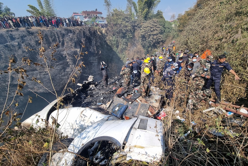 Plane crash in Nepal with 72 onboard. Workers inspect the crash site and debris